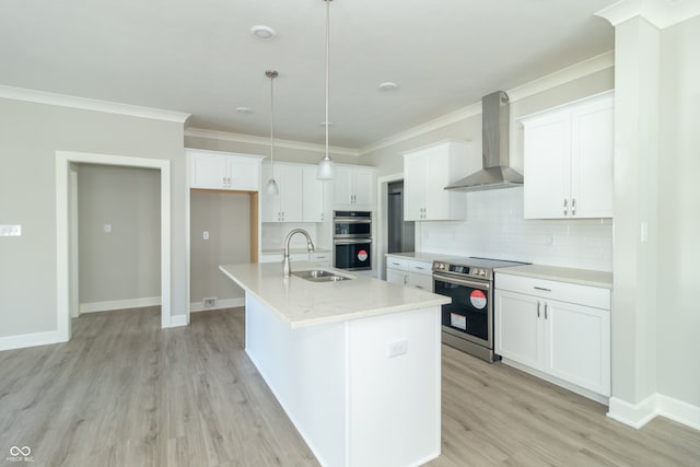 kitchen featuring appliances with stainless steel finishes, sink, wall chimney range hood, decorative light fixtures, and a center island with sink