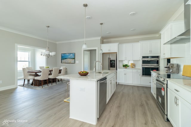 kitchen featuring appliances with stainless steel finishes, wall chimney exhaust hood, pendant lighting, a center island with sink, and white cabinets