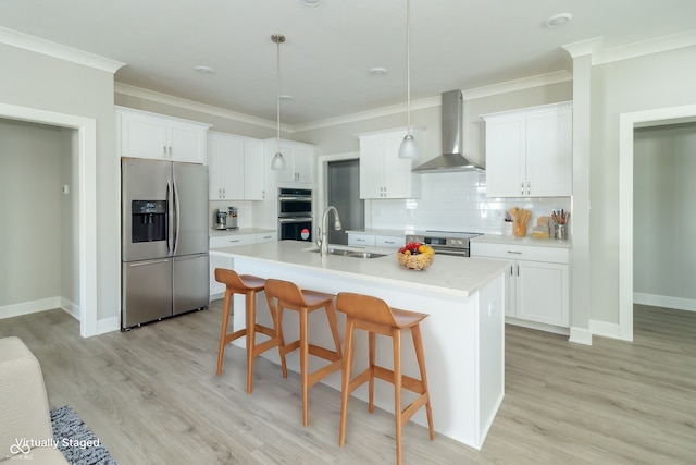 kitchen with stainless steel appliances, a kitchen island with sink, sink, wall chimney range hood, and pendant lighting