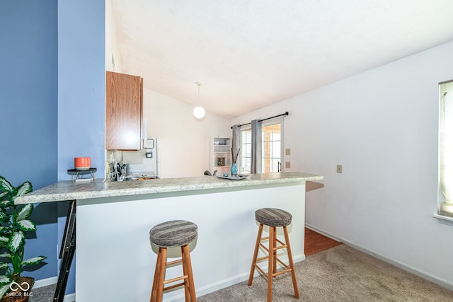 kitchen with light countertops, light carpet, a kitchen bar, a peninsula, and lofted ceiling