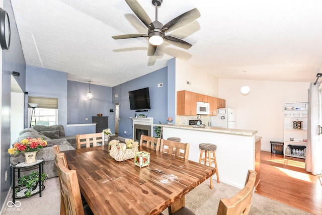 dining area featuring a textured ceiling, light wood-type flooring, vaulted ceiling, a fireplace, and a ceiling fan