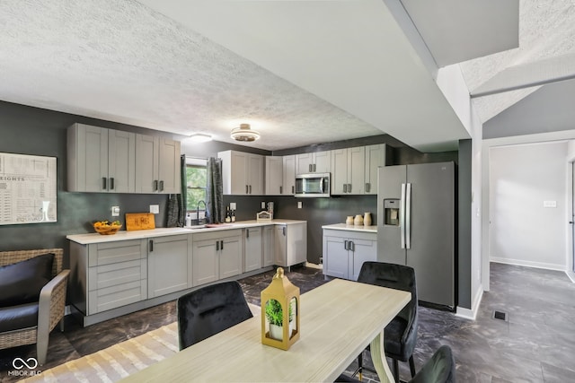 kitchen with a textured ceiling, vaulted ceiling, sink, gray cabinetry, and stainless steel appliances