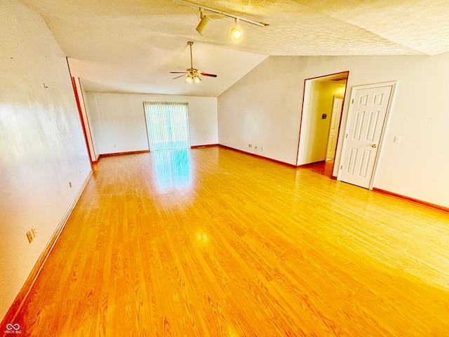 empty room featuring wood-type flooring, vaulted ceiling, rail lighting, a textured ceiling, and ceiling fan