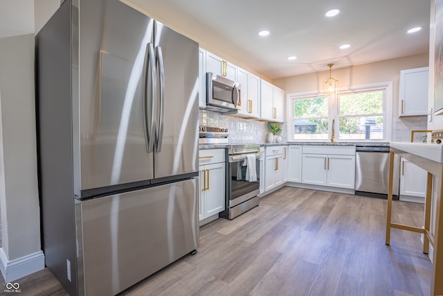 kitchen with stainless steel appliances, sink, light wood-type flooring, white cabinetry, and tasteful backsplash