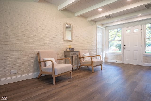 living area featuring dark wood-type flooring, brick wall, and beamed ceiling