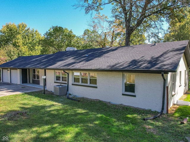 rear view of property featuring cooling unit, a garage, and a lawn