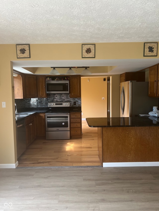 kitchen featuring light hardwood / wood-style floors, tasteful backsplash, sink, kitchen peninsula, and appliances with stainless steel finishes