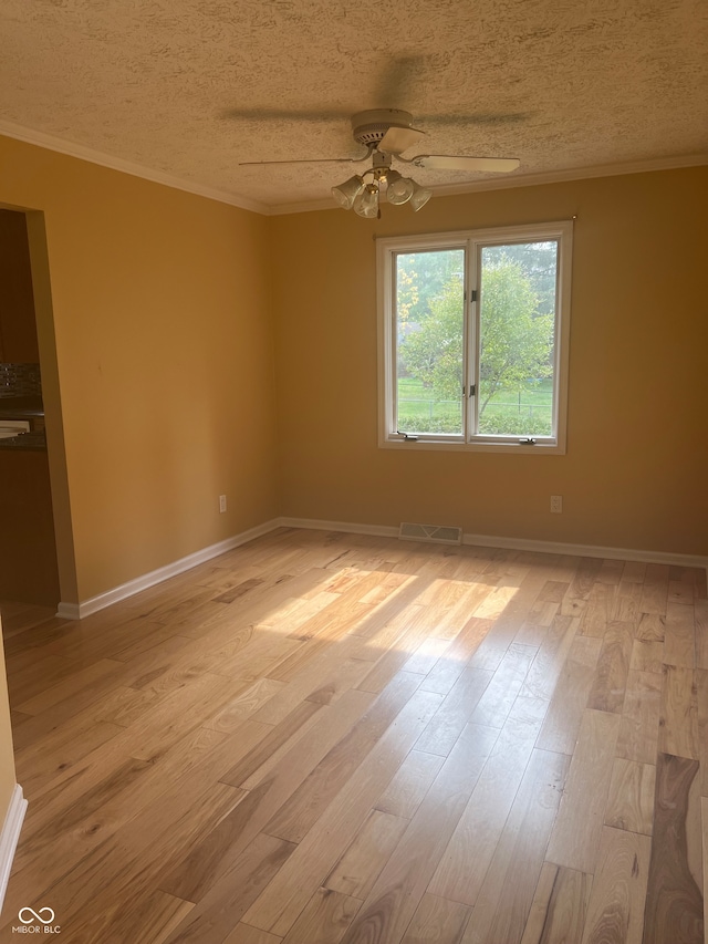 empty room with a textured ceiling, ceiling fan, ornamental molding, and light hardwood / wood-style flooring