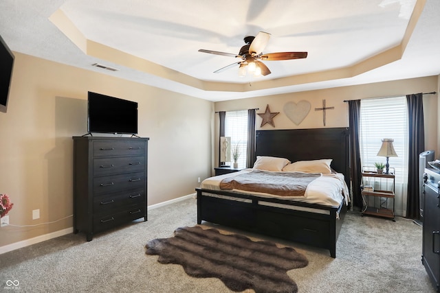 bedroom featuring a raised ceiling, light carpet, and ceiling fan