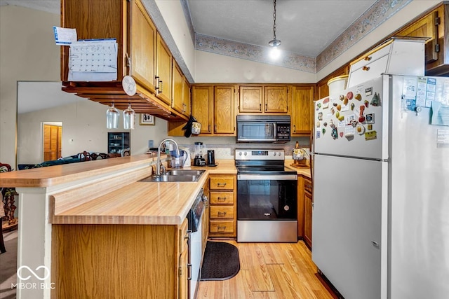 kitchen featuring lofted ceiling, light hardwood / wood-style flooring, kitchen peninsula, sink, and appliances with stainless steel finishes