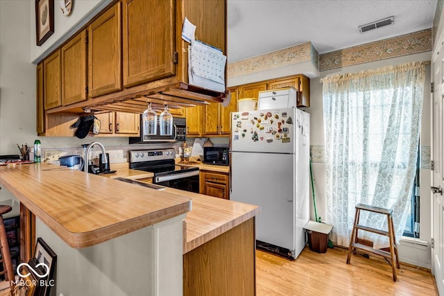 kitchen featuring light wood-type flooring, kitchen peninsula, stainless steel electric stove, white fridge, and a breakfast bar area