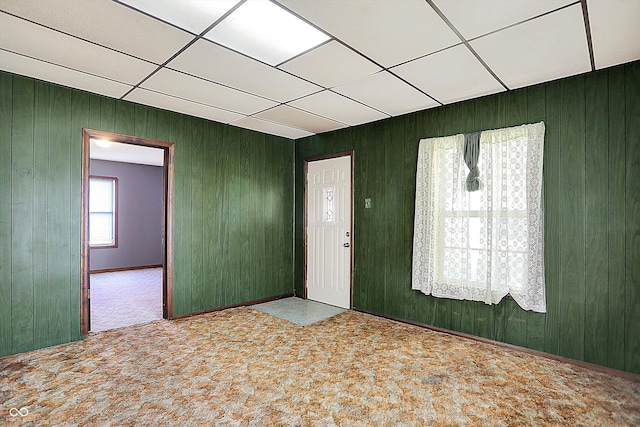 carpeted entryway featuring wood walls and a drop ceiling