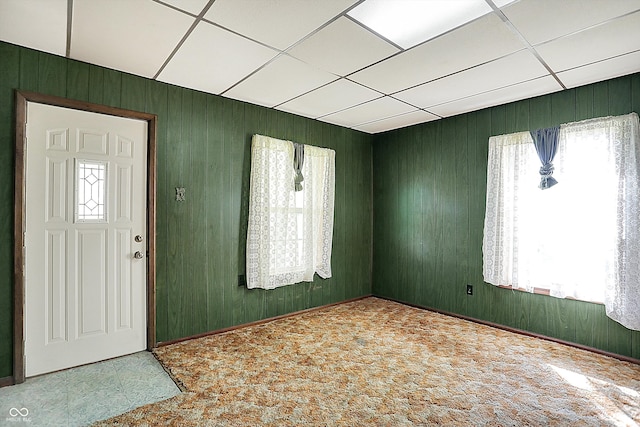 foyer entrance featuring a drop ceiling, plenty of natural light, and wood walls