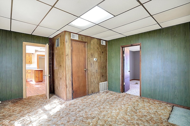 unfurnished bedroom featuring wooden walls, a paneled ceiling, carpet, a closet, and ensuite bathroom