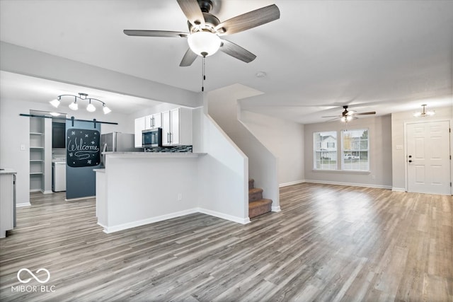 unfurnished living room with a barn door, light wood-type flooring, and ceiling fan