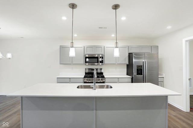 kitchen featuring stainless steel appliances, hanging light fixtures, and a center island with sink