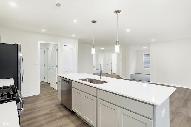 kitchen with a kitchen island with sink, sink, dark hardwood / wood-style floors, decorative light fixtures, and stainless steel appliances