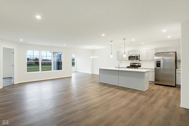 kitchen with a center island with sink, sink, hanging light fixtures, light wood-type flooring, and appliances with stainless steel finishes