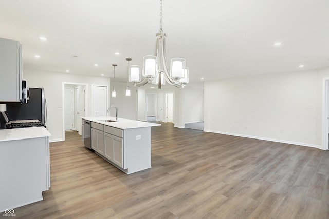 kitchen with gray cabinetry, a kitchen island with sink, sink, light hardwood / wood-style floors, and hanging light fixtures