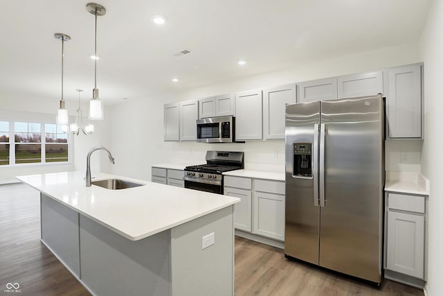 kitchen featuring a kitchen island with sink, hanging light fixtures, sink, light wood-type flooring, and appliances with stainless steel finishes