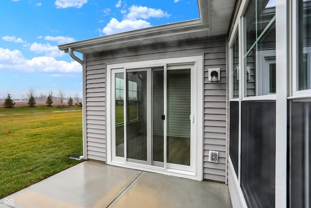 view of exterior entry with a lawn and a patio area