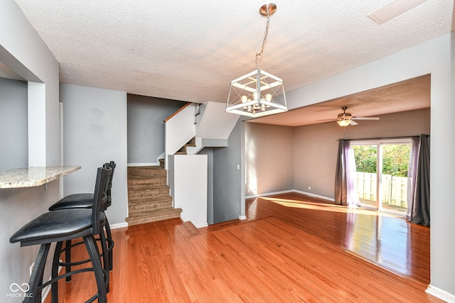 dining room with hardwood / wood-style floors, a textured ceiling, and ceiling fan with notable chandelier