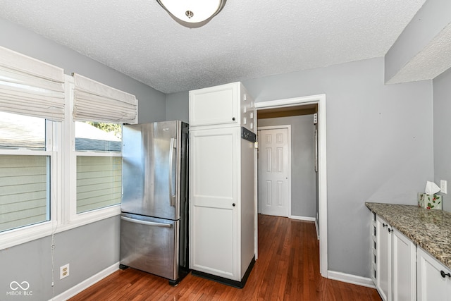 kitchen with dark hardwood / wood-style flooring, white cabinets, stone counters, and stainless steel refrigerator