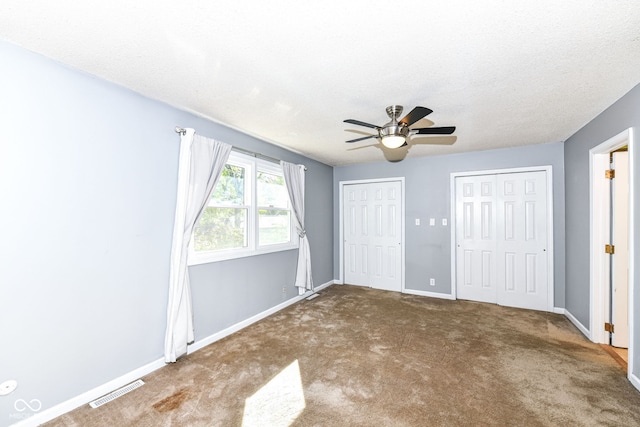 unfurnished bedroom featuring ceiling fan, carpet, and two closets