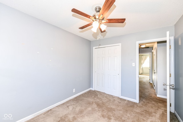 unfurnished bedroom with a textured ceiling, light colored carpet, a closet, and ceiling fan