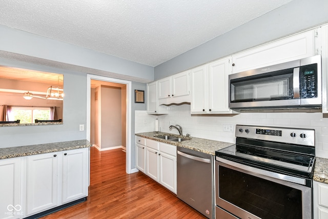 kitchen with appliances with stainless steel finishes, sink, backsplash, white cabinetry, and light hardwood / wood-style flooring