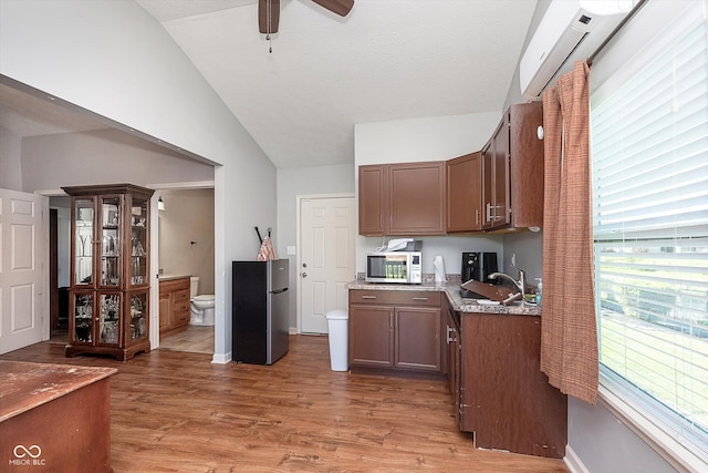 kitchen with stainless steel appliances, wood-type flooring, lofted ceiling, sink, and light stone countertops