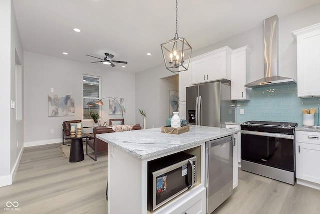 kitchen featuring a center island, wall chimney range hood, light wood-type flooring, white cabinetry, and stainless steel appliances