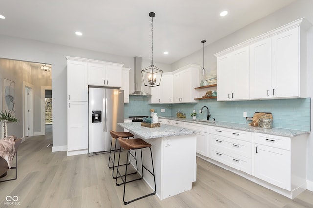 kitchen featuring white cabinetry, a center island, wall chimney range hood, stainless steel fridge, and light hardwood / wood-style floors