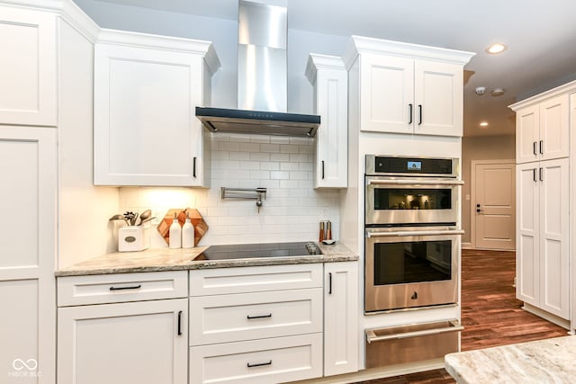 kitchen featuring double oven, black electric stovetop, wall chimney exhaust hood, dark wood-type flooring, and white cabinetry