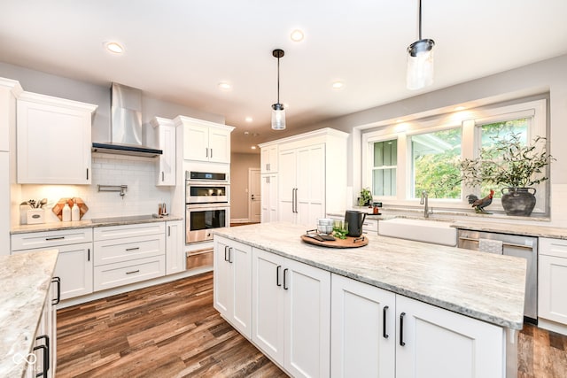 kitchen featuring wall chimney range hood, appliances with stainless steel finishes, white cabinetry, and pendant lighting