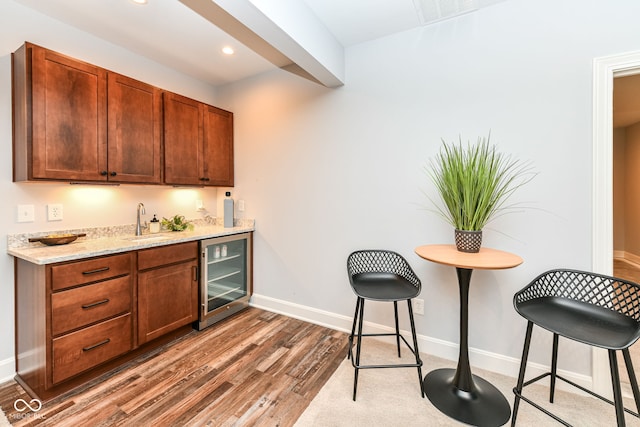 kitchen with wine cooler, sink, light wood-type flooring, and a kitchen breakfast bar