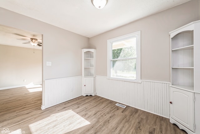 empty room with ceiling fan, light wood-type flooring, built in features, and a textured ceiling