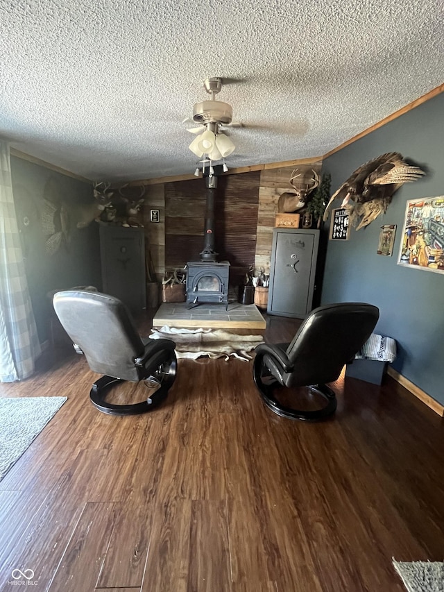 living room with a wood stove, ceiling fan, wood-type flooring, a textured ceiling, and wooden walls