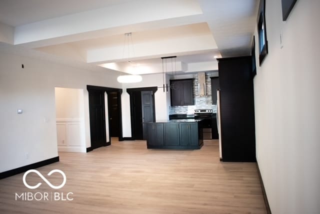 kitchen featuring stainless steel range with electric stovetop, a tray ceiling, light wood-type flooring, and tasteful backsplash