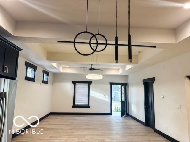 empty room with ceiling fan, a tray ceiling, and light wood-type flooring