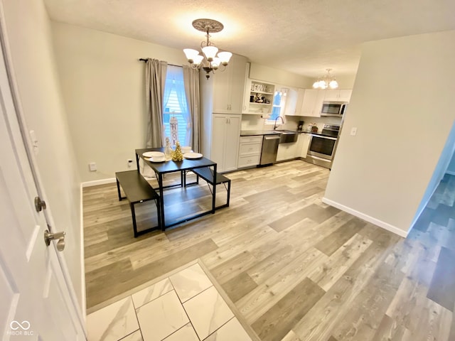 kitchen with white cabinetry, an inviting chandelier, light wood-type flooring, decorative light fixtures, and appliances with stainless steel finishes