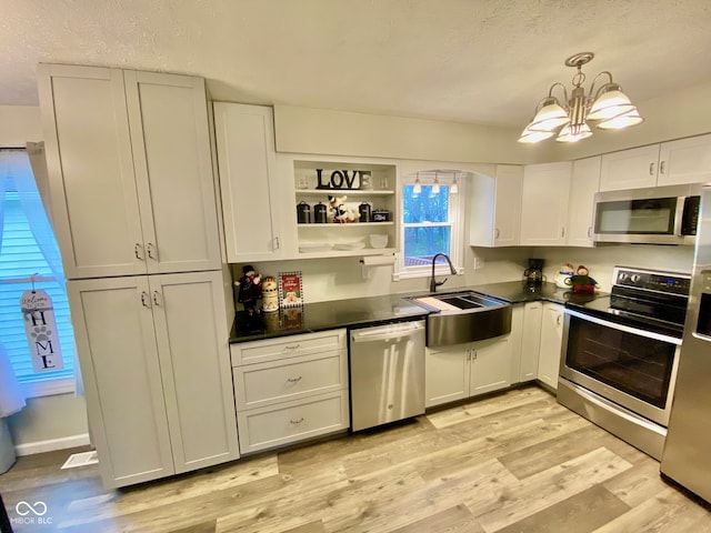 kitchen with sink, decorative light fixtures, light wood-type flooring, appliances with stainless steel finishes, and a notable chandelier