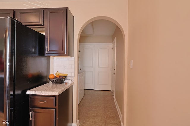 kitchen featuring stainless steel fridge, dark brown cabinets, and decorative backsplash