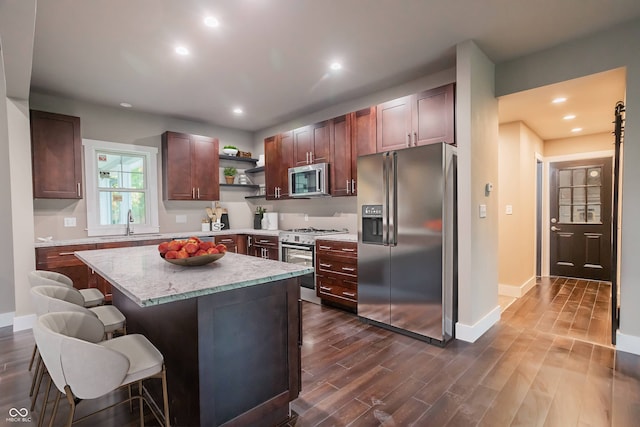 kitchen with dark wood-type flooring, a center island, a breakfast bar, appliances with stainless steel finishes, and sink