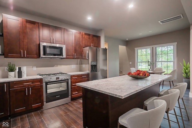 kitchen featuring a kitchen island, appliances with stainless steel finishes, light stone counters, and a breakfast bar area