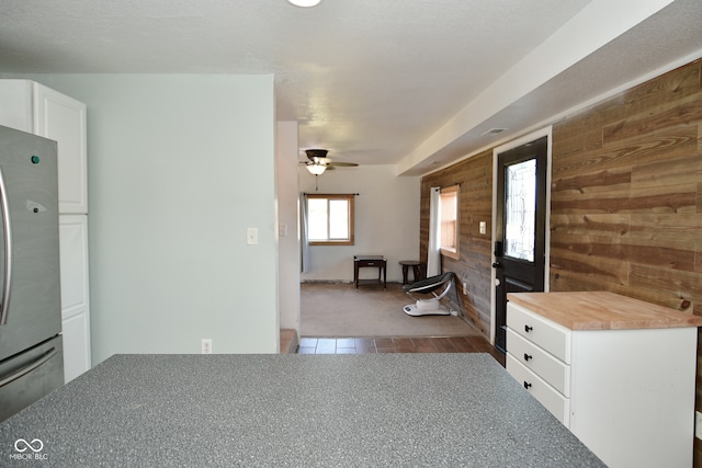 kitchen with ceiling fan, white cabinetry, stainless steel refrigerator, wood walls, and dark tile patterned flooring