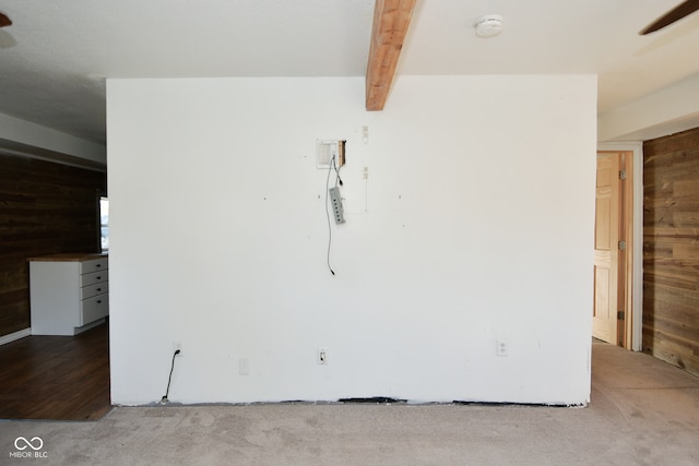 empty room with beam ceiling, wooden walls, carpet flooring, and ceiling fan