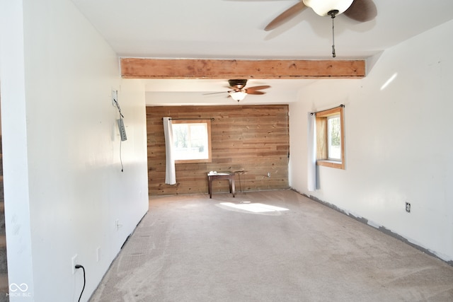 spare room with beam ceiling, wood walls, a wealth of natural light, and carpet floors