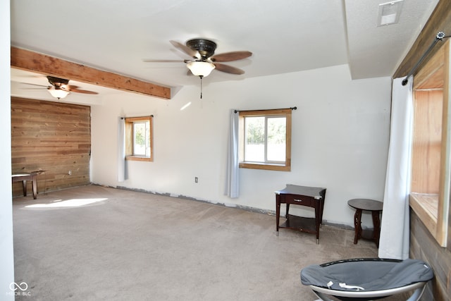 interior space with wood walls, beam ceiling, light carpet, and plenty of natural light