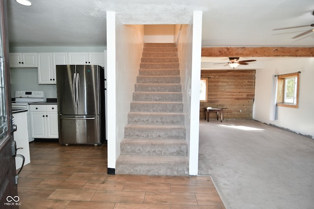 staircase featuring beamed ceiling, carpet, ceiling fan, a textured ceiling, and wood walls